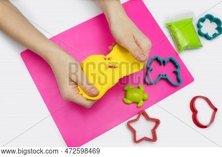 A Child Plays With Soft Yellow Plasticine On A Pink Board. The Hands Of The Child Hold Air Plasticin