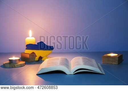Christian Holy Bible With сandles Lighting On Blue Background. Pray For Ukraine Concept
