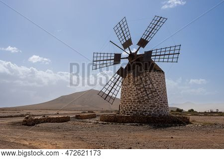 Old Traditional Windmill, Located In A Stone Desert. Blue Sky With Some White Clouds In The Winter. 