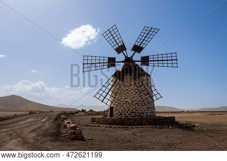 Old Traditional Windmill, Located In A Stone Desert. Blue Sky With Some White Clouds In The Winter. 