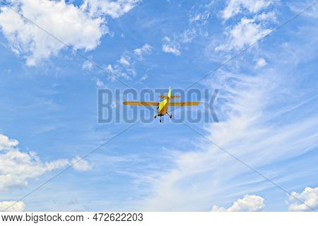Yellow Single-engine Ultralight Airplane Flying In The Blue Sky With White Clouds