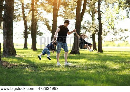 Fathers Day. Happy Dad Having Fun And Spins Two Kids Outdoors. Single Daddy With Little Son And Daug