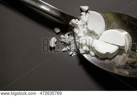 Pharmaceutical medicine drugs powder on a silver metal spoon. Smashed remedy, tablets, on top of a g