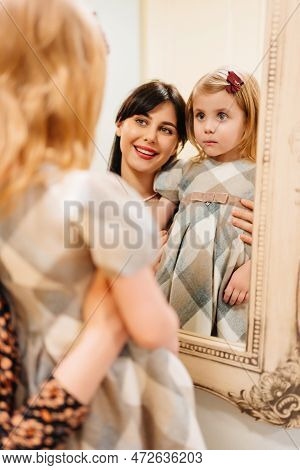A Cute Little Girl In A Plaid Dress And Mom Looks In The Mirror And Primping.