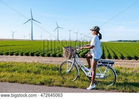 Young Woman Electric Green Bike Bicycle By Windmill Farm , Windmills Isolated On A Beautiful Summer