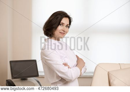 Positive Confident Female Doctor Posing In Doctor's Smock With Hands Folded In Front Against Intence