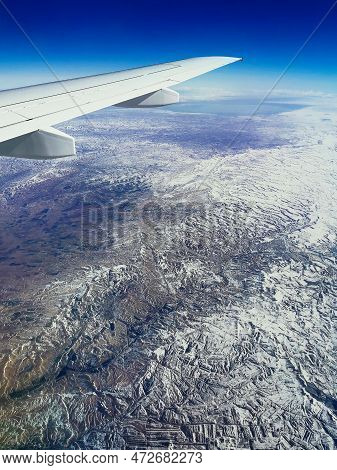 Aerial View Through Porthole Of Plane To Of Snow-covered Mountain. Scenic View Through Aircraft. Air