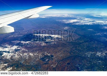 Aerial View Through Porthole Of Plane To Of Snow-covered Mountain. Scenic View Through Aircraft. Air