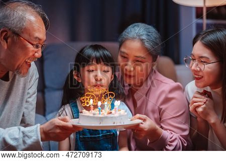 Asian Happy Family Of Little Girl Blowing Out Candles On Cake. Celebrate Birthday Anniversary Party