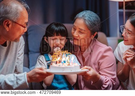 Asian Happy Family Of Little Girl Blowing Out Candles On Cake. Celebrate Birthday Anniversary Party 