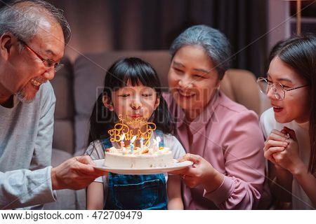 Asian Happy Family Of Little Girl Blowing Out Candles On Cake. Celebrate Birthday Anniversary Party 