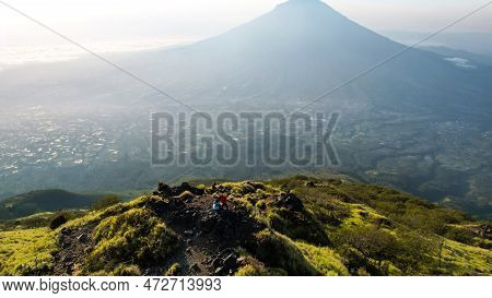 Asian Man Standing On Top Of A Nearby Mountain Looking At Mount Sindoro. West Java, Indonesia, March