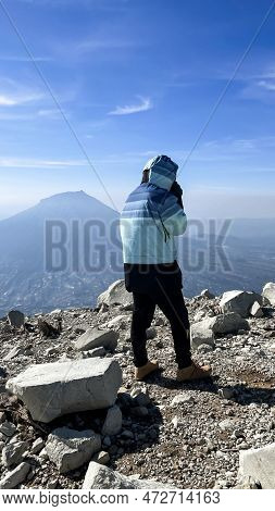 Asian Man Standing On Top Of A Nearby Mountain Looking At Mount Sindoro. West Java, Indonesia, March
