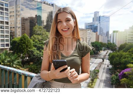 Portrait Of Young Brazilian Woman Holding Mobile Phone Looks At Camera, Sao Paulo, Brazil