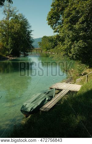 Jetty With A Covered Boat Beside It Near The Crystal-clear Water At The Mangfall River In Germany