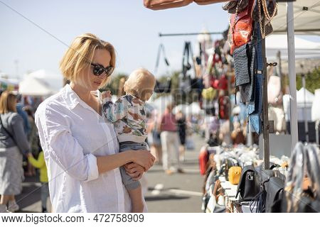 Mother Hoding His Infant Baby Boy Child Whilechecing Items At Sunday Flea Market