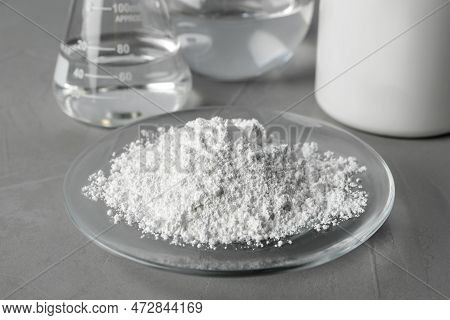 Plate With Calcium Carbonate Powder And Laboratory Glassware On Grey Table, Closeup