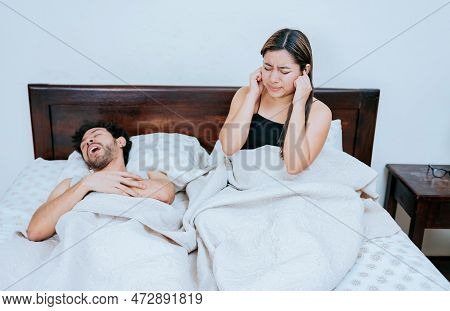 Husband Snoring While The Wife Suffers And Covers Her Ears. Sleep Apnea Concept, Snoring Man In Bedr