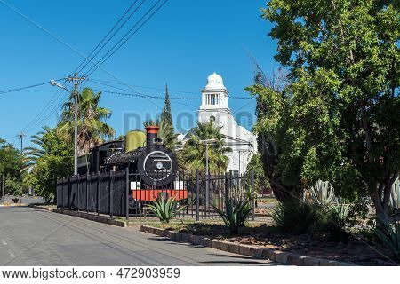 Fauresmith, South Africa - Feb 21, 2023: Historic steam locomotive in Fauresmith, one of only a few towns on earth where the railway line runs down the centre of the main road. Town Hall visible in the back
