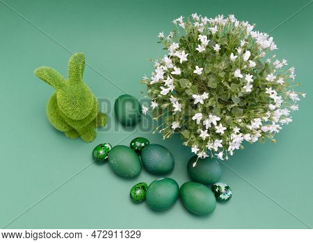 Easter Green Hare With Blue Colored Chicken Quail Eggs On Blue Background. White Spring Flowers In P