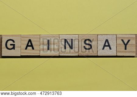The Word Gainsay Of Gray Small Wooden Letters Lies On A Yellow Table