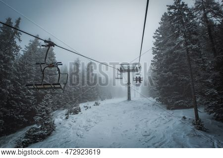 Ski Lift Transports Skiers And Snowboarders In Foggy Day At Snowy Mountain. Frozen Funicular. Pinzol