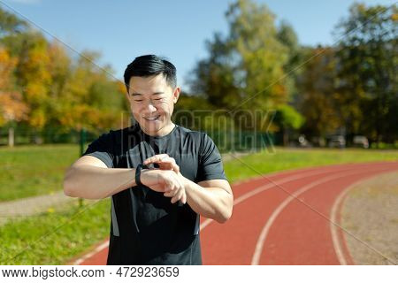 An Asian Man, An Athlete Standing On A Running Track In A Stadium, Looking And Checking The Time On 