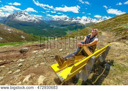 Woman Resting On Yellow Bench On Top Of Muottas Muragl Mountain Of Funicular Railway In Switzerland.
