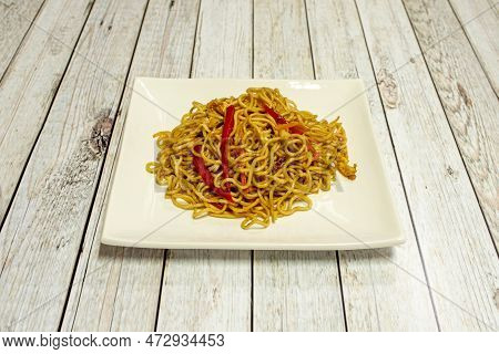 Sauteed Noodles With Vegetables And Strips Of Red Peppers With Soy Sauce On White Square Plate