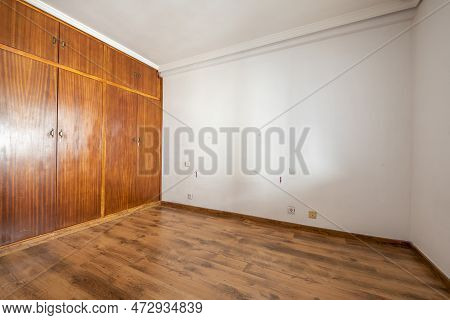 Empty Room With Built-in Wardrobe With Old Sapele Wood Doors And Dark Wooden Floors