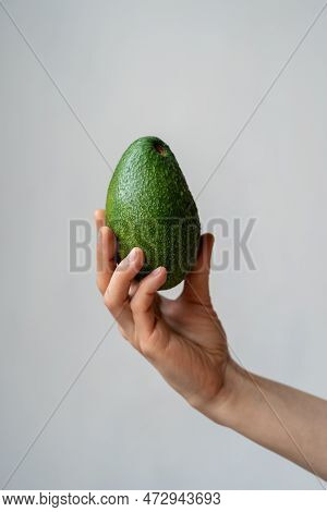 Human Hand Holding Green Ripe Organic Avocado Against Grey Wall. Healthy Vegetarian Food. Nutrient-d