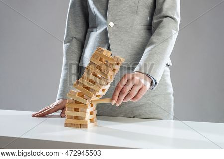 Businesswoman Removing Wooden Block From Falling Tower On Table. Management Of Risks And Economic In