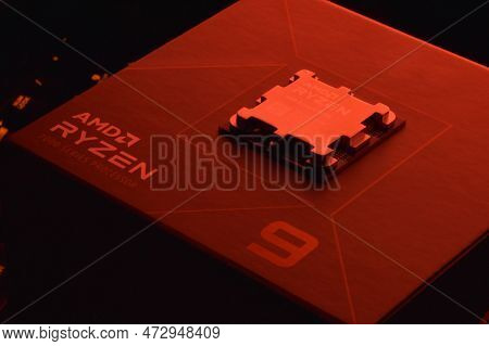 A Close-up Of An Amd Ryzen 9 7900X Processor In A Packaging Box With Backlit Keyboards In The Backgr