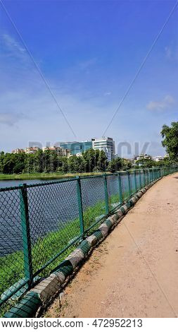 Walking Lane Of Iblur Lake With Green Cover And Clear Cloudy Skyn And Cityscape Infrastructure.