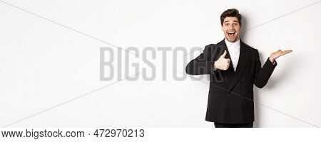 Portrait Of Hadnsome Bearded Man In Formal Suit, Showing Thumb-up And Holding Product In Hand Over W