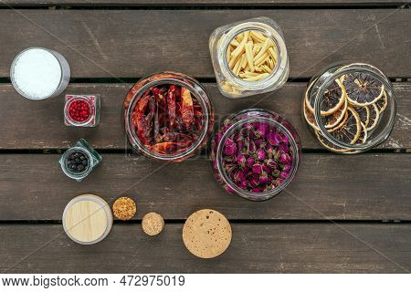Set Of Glass Jars With Cork Lids Filled With Seasonings And Dried Tea Roses On Unvarnished Dark Wood