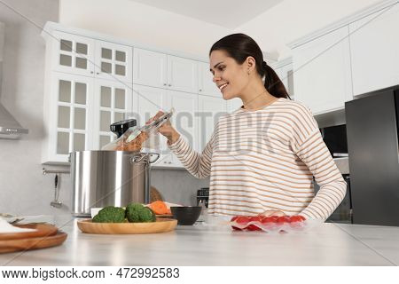 Woman Putting Vacuum Packed Meat Into Pot With Sous Vide Cooker In Kitchen. Thermal Immersion Circul