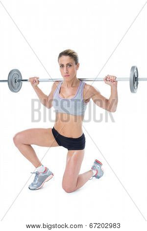 Strong female crossfitter lifting barbell behind head looking at camera on white background
