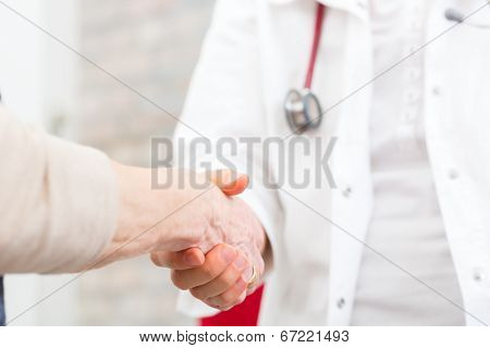 Doctor giving pensioner in surgery comfort and consoling with holding hands 