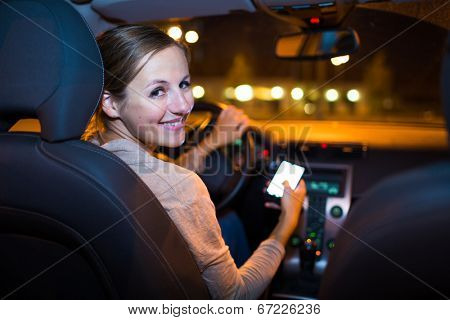 Pretty young woman using her smart phone while driving her car at night