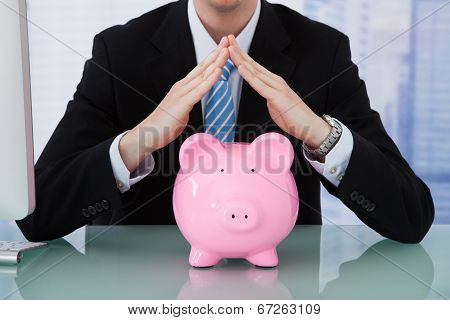 Businessman Protecting Piggy Bank At Desk