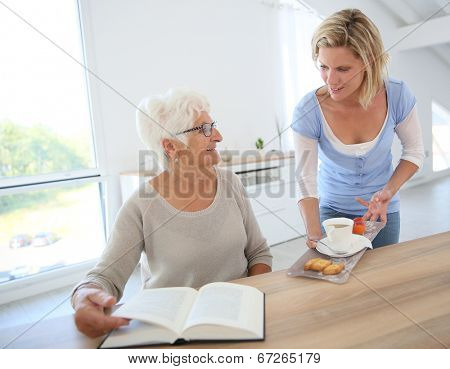 Home helper giving tea to elderly woman