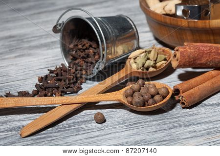 Cardamon, clove and pepper in spoons on wooden background with various spices - cinnamon, ginger and nutmeg