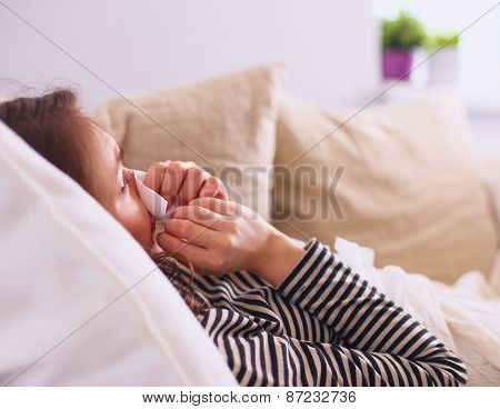 Portrait of a sick woman blowing her nose while sitting on the sofa