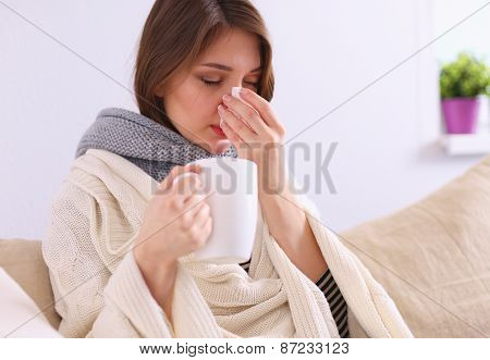 Portrait of a sick woman blowing her nose while sitting on the sofa