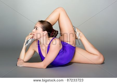 Young Female Contortionist In Purple Leotard On Dark Background