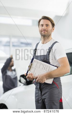 Portrait of confident male automobile mechanic with clipboard in car repair store