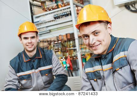 Happy young electrician builder workers in front of fuseboard