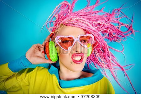 Crazy expressive trendy DJ girl in bright clothes, headphones and bright dreadlocks. Disco, party. Bright fashion.