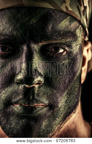 Close-up portrait of a brave soldier in war paint looking at camera. Black background. Military, war. Special forces.